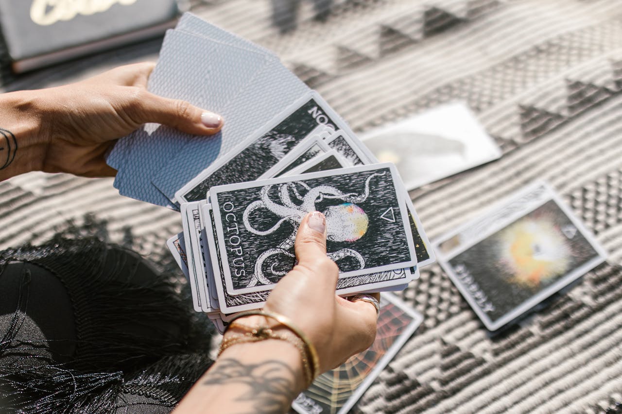 Hands holding tarot cards during a reading session on a patterned mat.